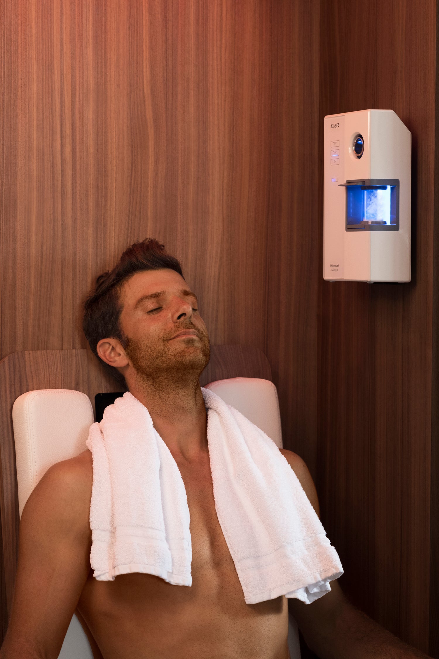 Man lying in a sauna with a towel draped over his shoulders, surrounded by wooden walls.