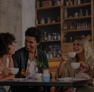 Three friends laughing and enjoying drinks at a cafe.