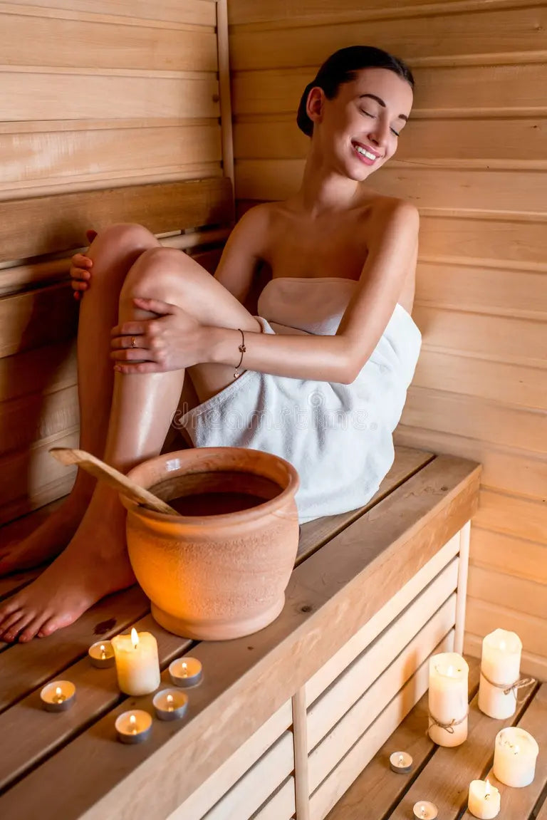 Woman in a sauna with a pot of water and candles around her